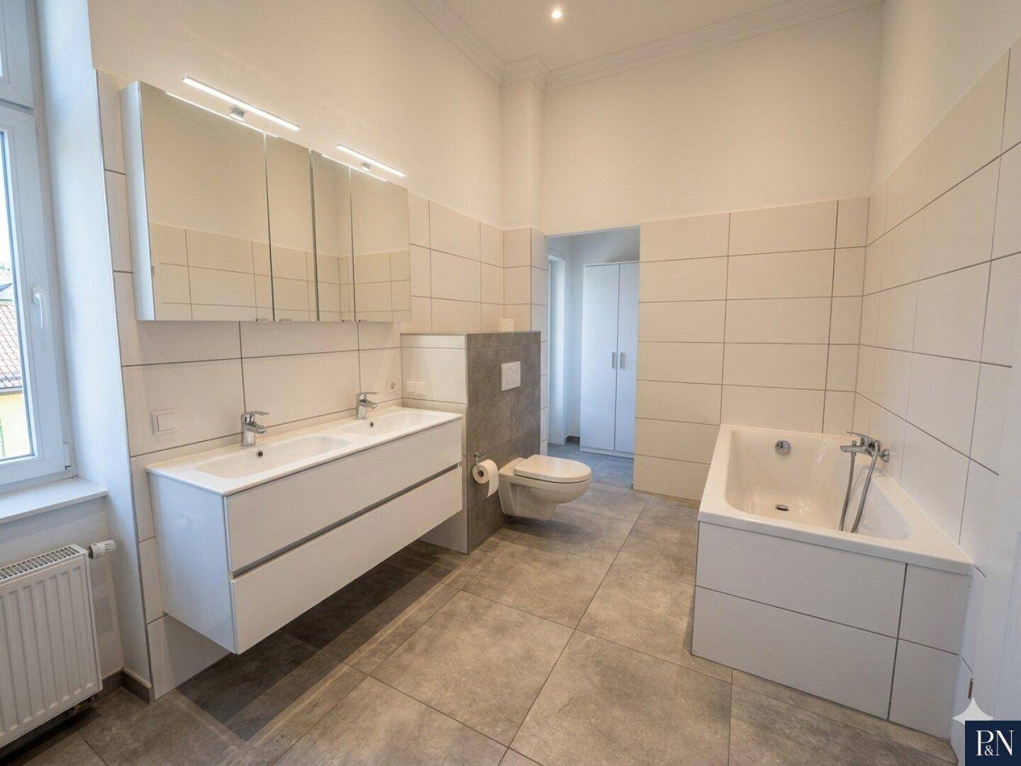 Elegantes Badezimmer mit Doppelwaschbecken, Badewanne und wandhängendem WC.