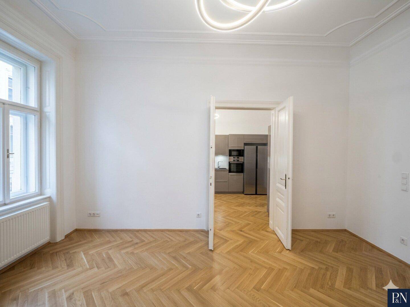 Großzügiges Zimmer mit Fischgrätparkett und Stuckdecke, mit direktem Zugang zur modernen Küche.