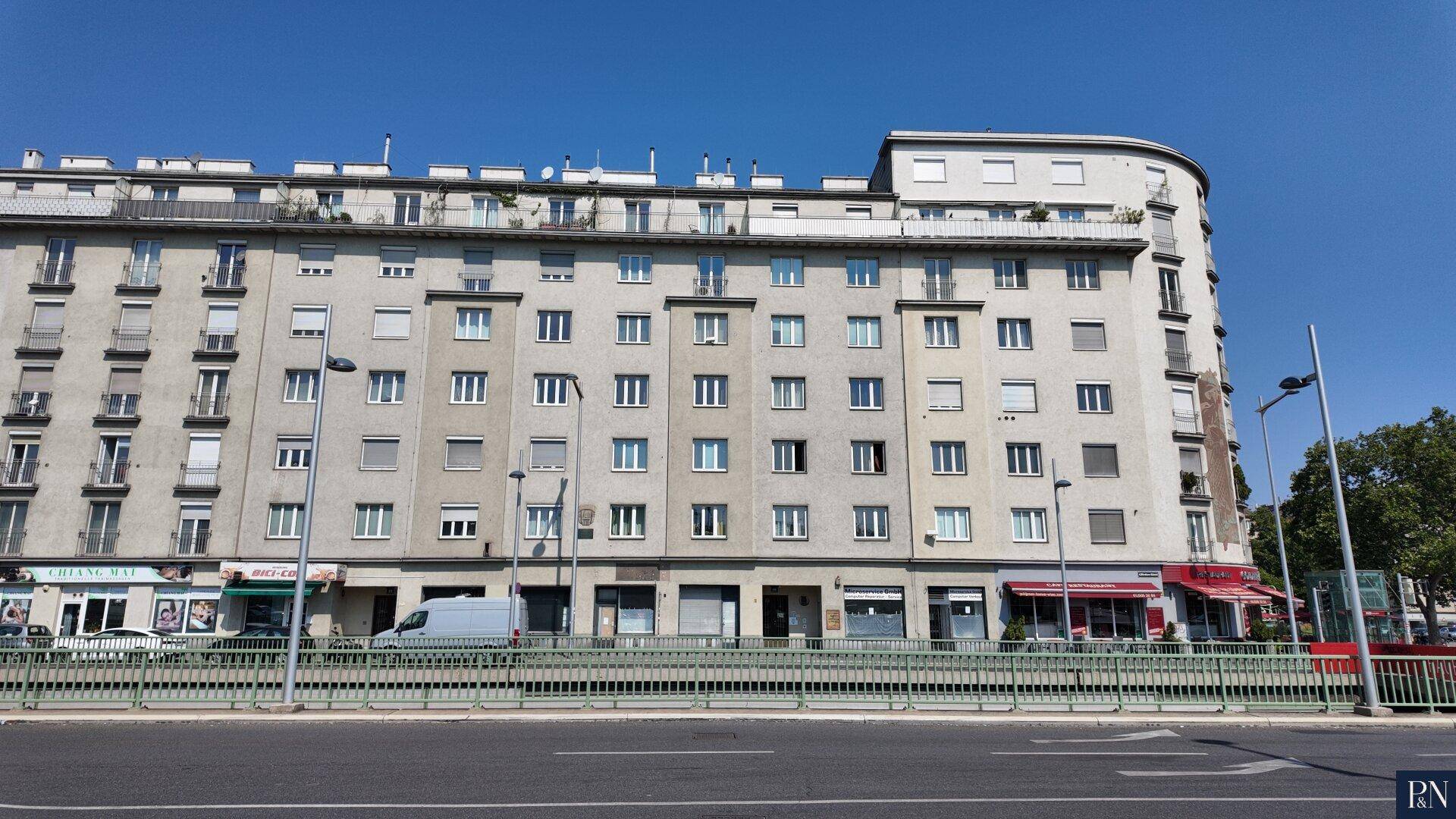 Großes Wohngebäude mit vielen Fenstern und Geschäften im Erdgeschoss an einer Straße.