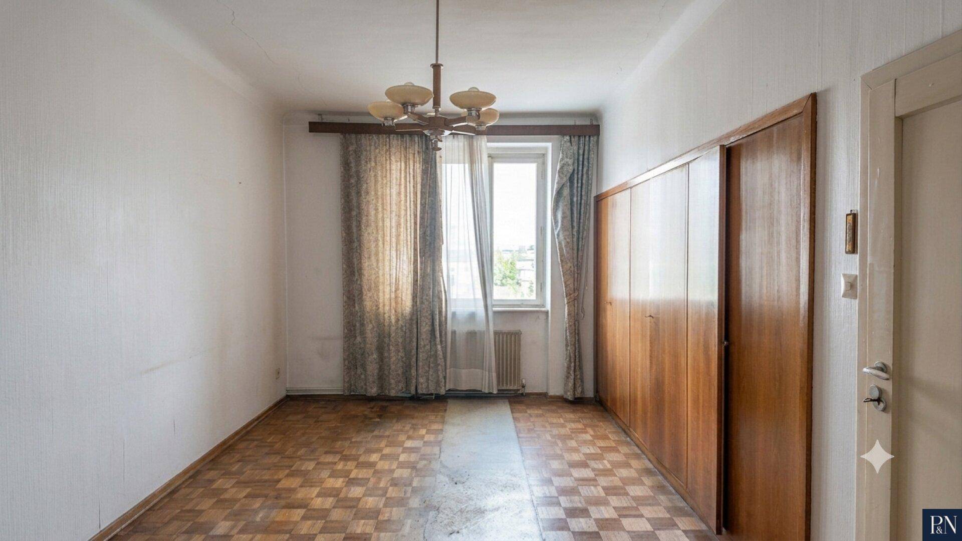 Leeres Zimmer mit Parkettboden, Einbauschränken und Fenster mit Vorhängen.