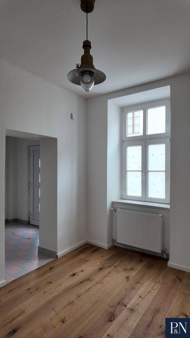 Eingangsbereich mit Fliesenboden, der zu einem Raum mit Holzboden und Fenster führt.