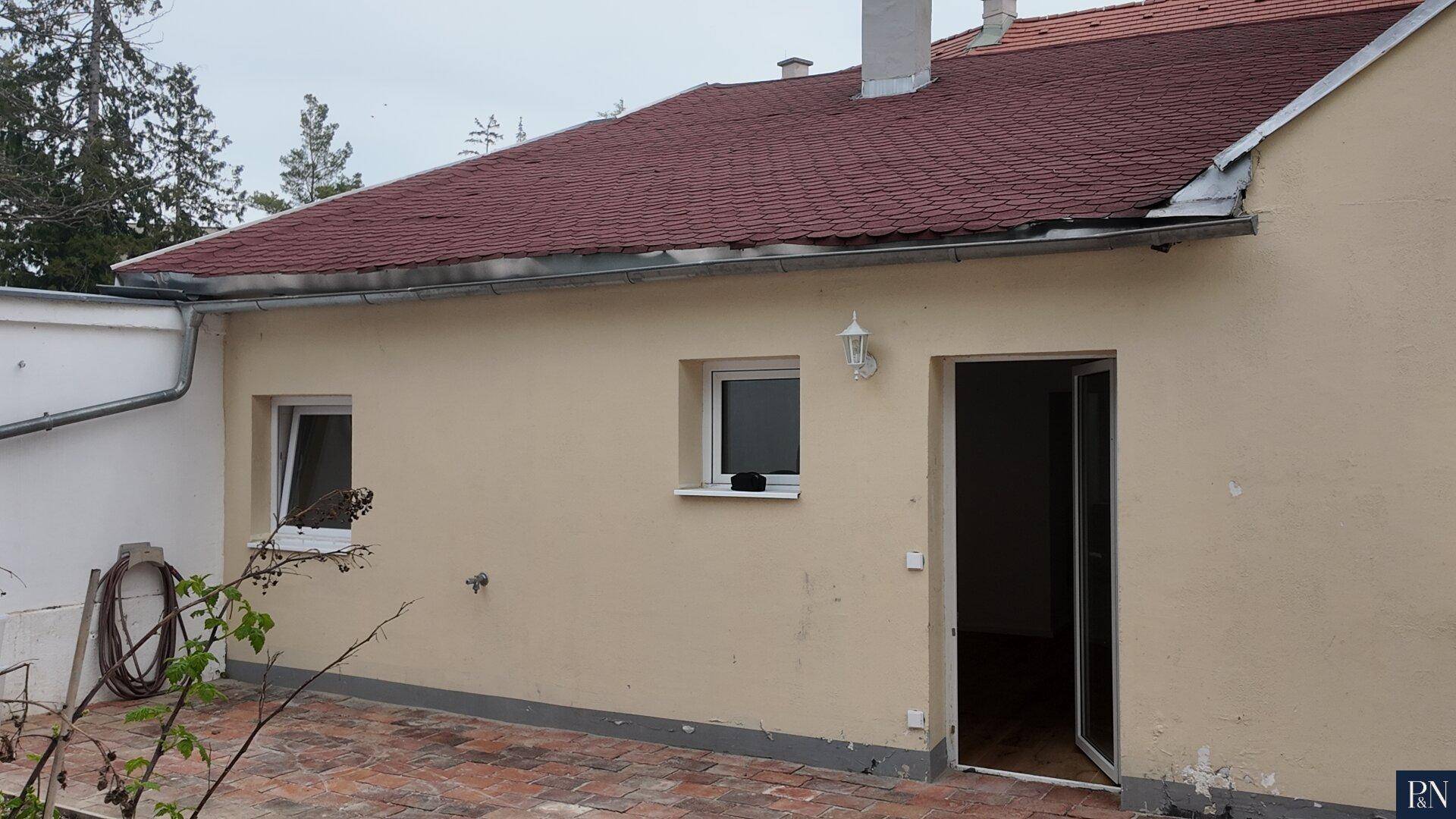 Hinterhof mit gepflasterter Terrasse und Zugang zum Haus, umgeben von einer Mauer.