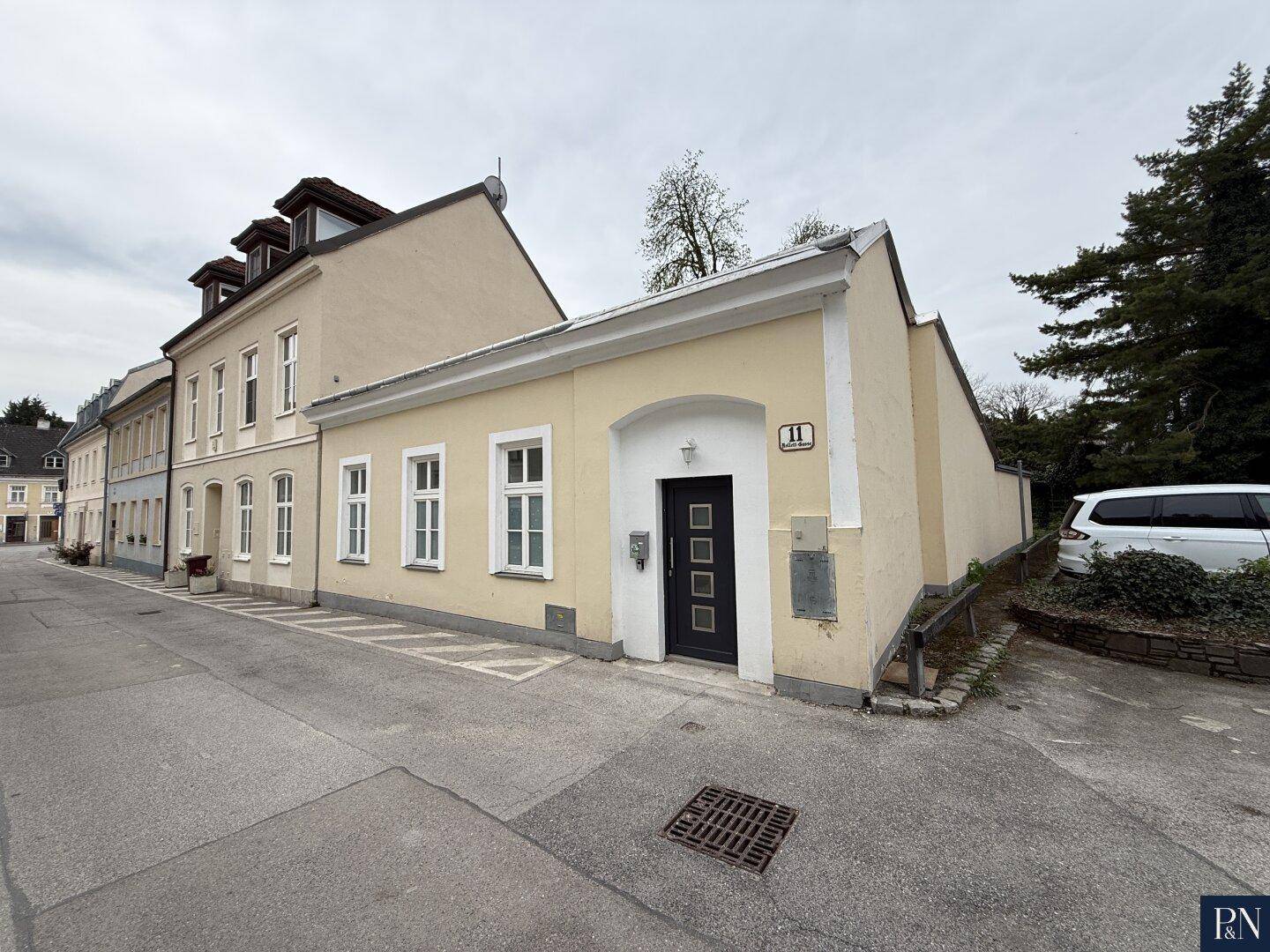 Außenansicht eines charmanten Gebäudes mit gelber Fassade und dunkler Eingangstür an der Straße.