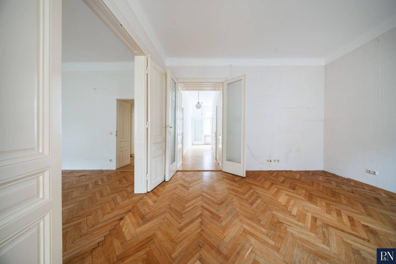 Langer Flur mit Fischgrätparkett und hohen Türen, der mehrere Zimmer miteinander verbindet.