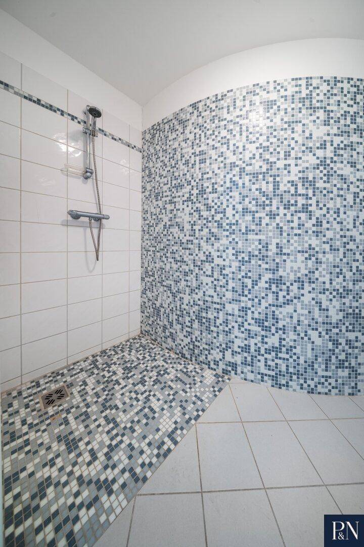 Detaillierte Ansicht der modernen Mosaikdusche im Badezimmer mit weißen Fliesen.