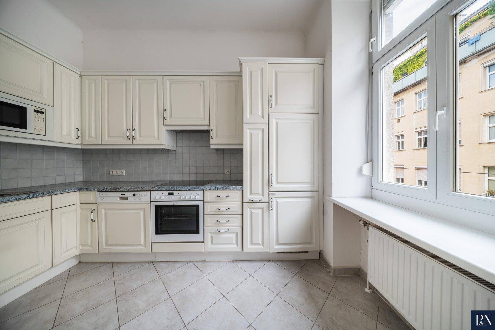 Traditionelle Einbauküche mit cremefarbenen Schränken, Granitarbeitsplatte und Fenster.