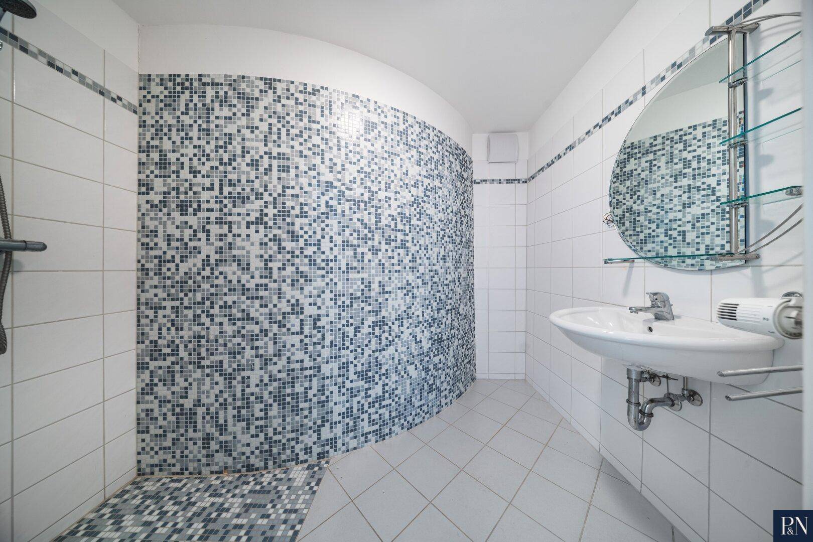 Modern gefliestes Badezimmer mit Mosaikdusche, Einzelwaschbecken und rundem Spiegel.