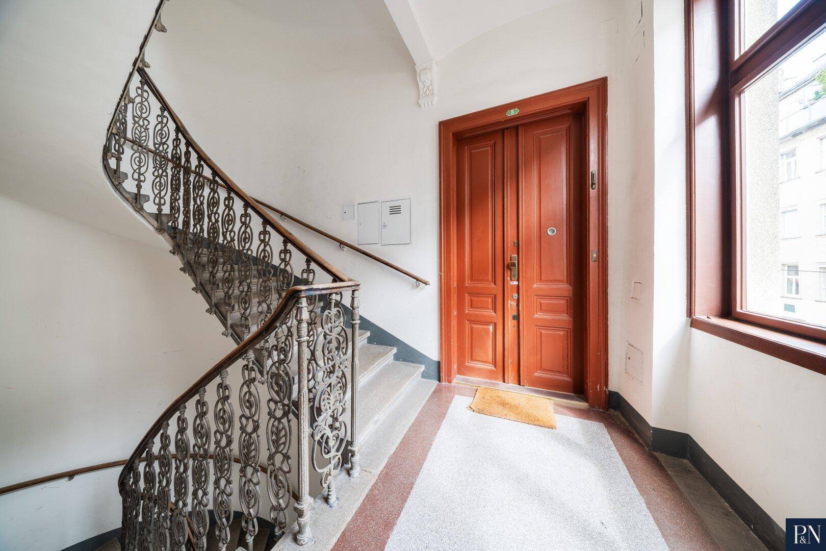 Historisches Treppenhaus mit schmiedeeisernem Geländer und einer großen Holztür zum Apartment.