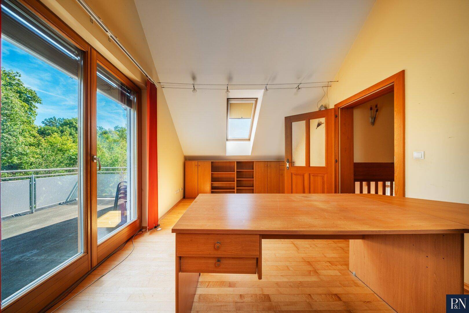 Geräumiges Arbeitszimmer im Dachgeschoss mit Holzboden, Dachfenster und Balkonzugang.