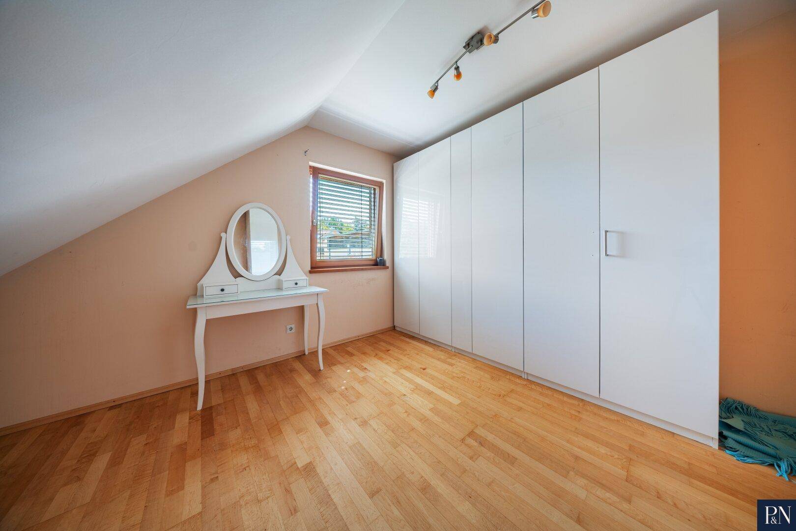 Schlafzimmer mit Dachschräge, Parkettboden und großem weißen Einbauschrank.