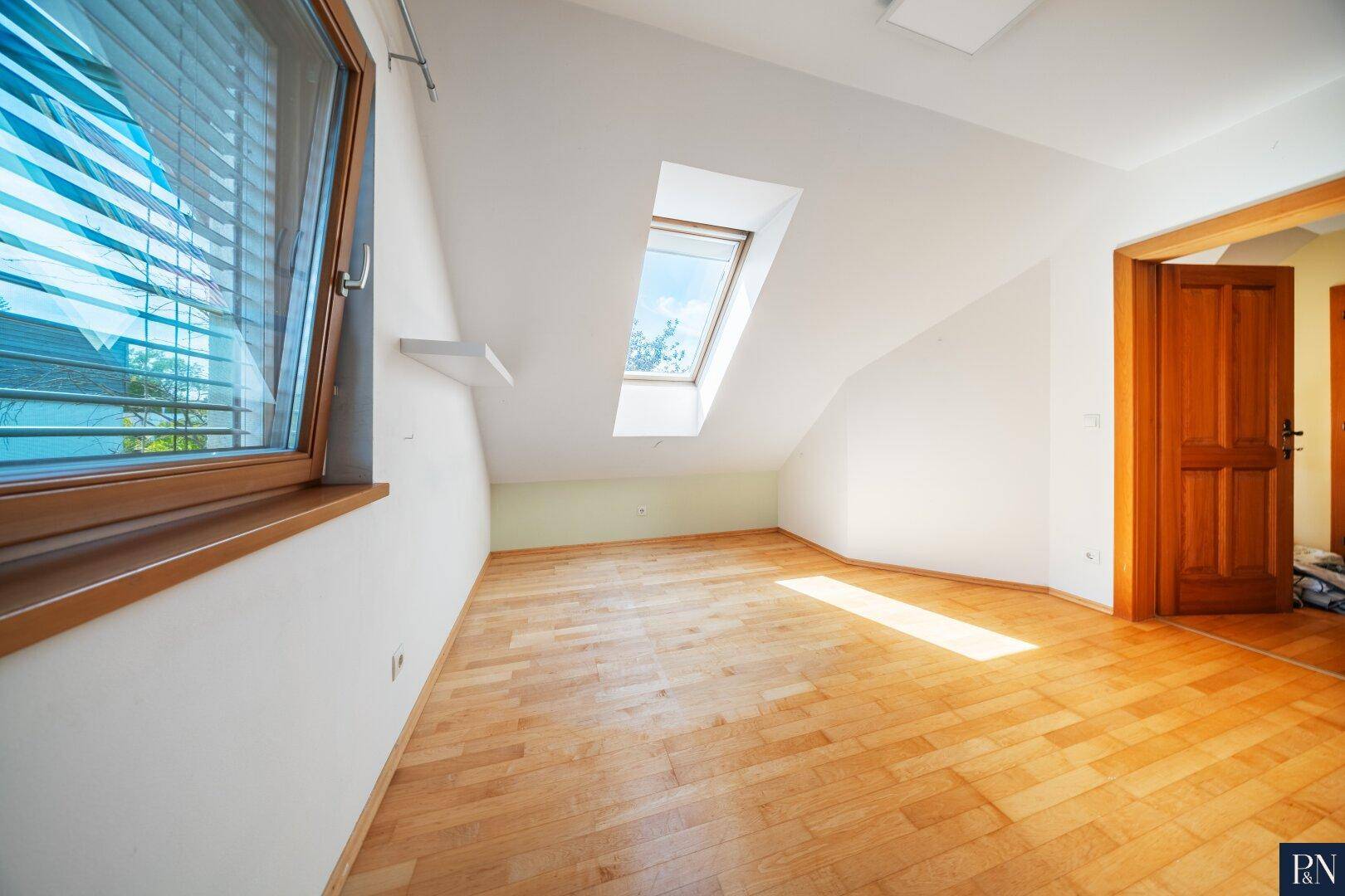 Lichtdurchflutetes Schlafzimmer mit Parkettboden, Dachschräge und Fenster mit Jalousien.