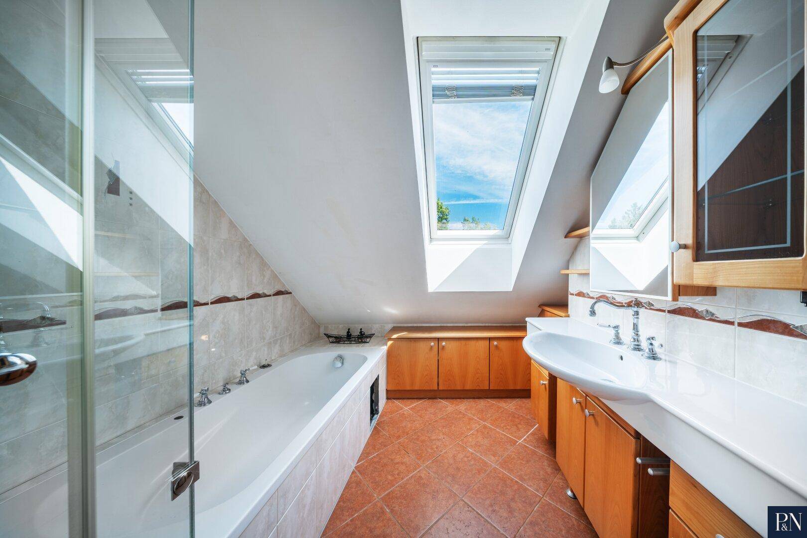 Badezimmer im Dachgeschoss mit Badewanne, Waschtisch und großem Dachfenster.
