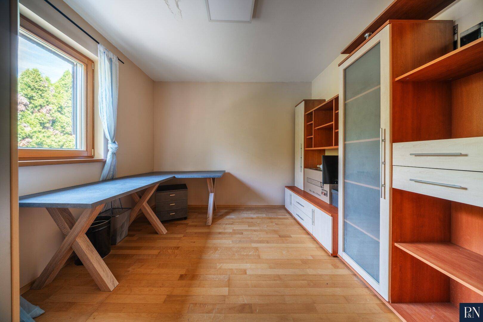 Geräumiges Zimmer mit Parkettboden, großem Fenster und integrierten Regalsystemen.