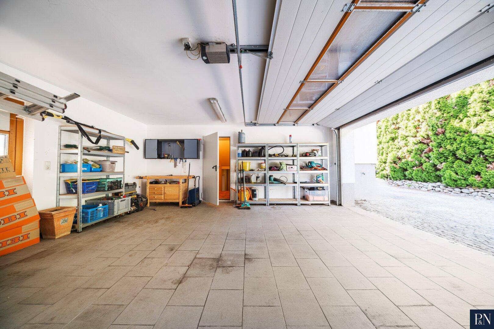 Geräumige Garage mit Fliesenboden, Regalen und direktem Zugang nach draußen.