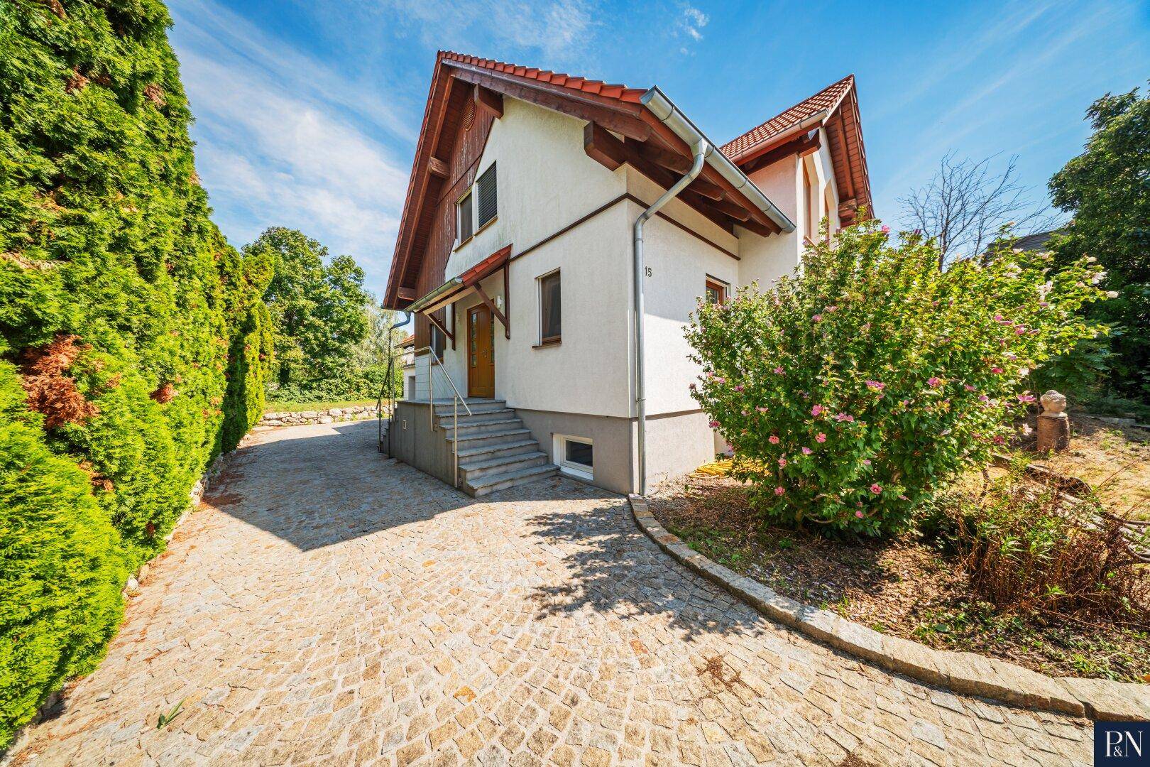 Seitenansicht des Einfamilienhauses mit gepflasterter Auffahrt und grüner Hecke.