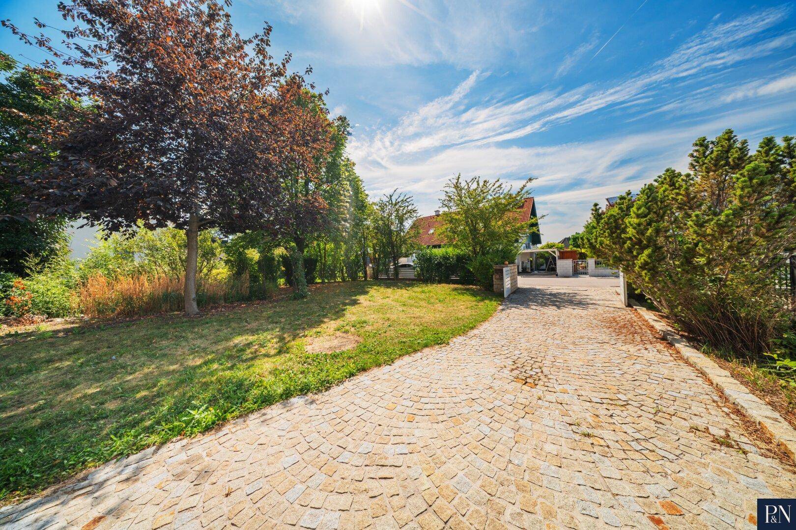 Lange gepflasterte Auffahrt führt durch den grünen Garten zum Haus.
