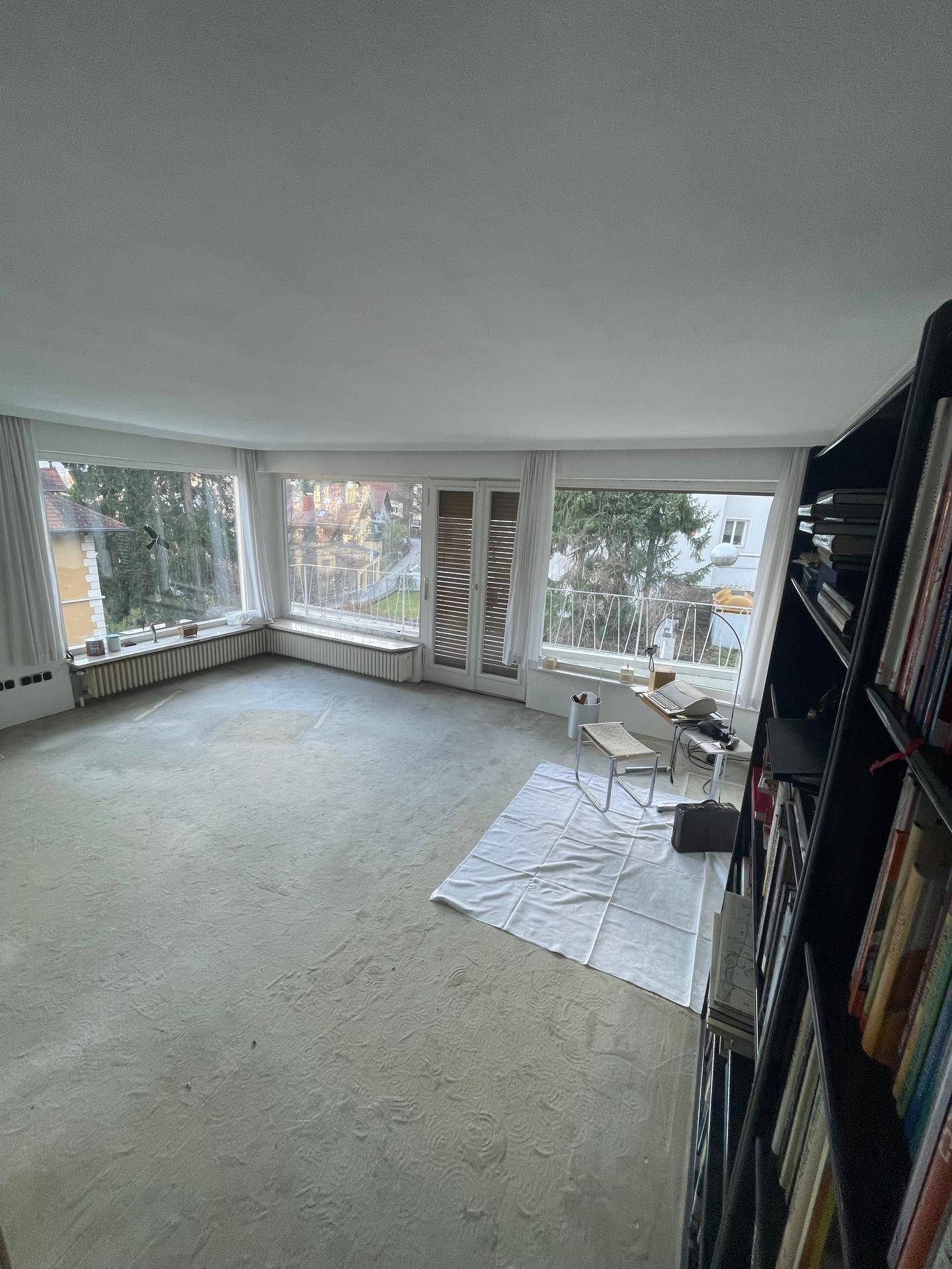 Geräumiges Wohnzimmer mit Teppichboden, großen Erkerfenstern und Blick auf die Umgebung.