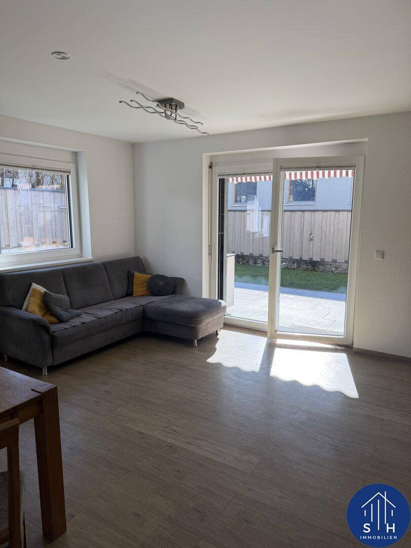 Gemütliches Wohnzimmer mit grauem Sofa, hellem Holzboden und direktem Zugang zum Garten.
