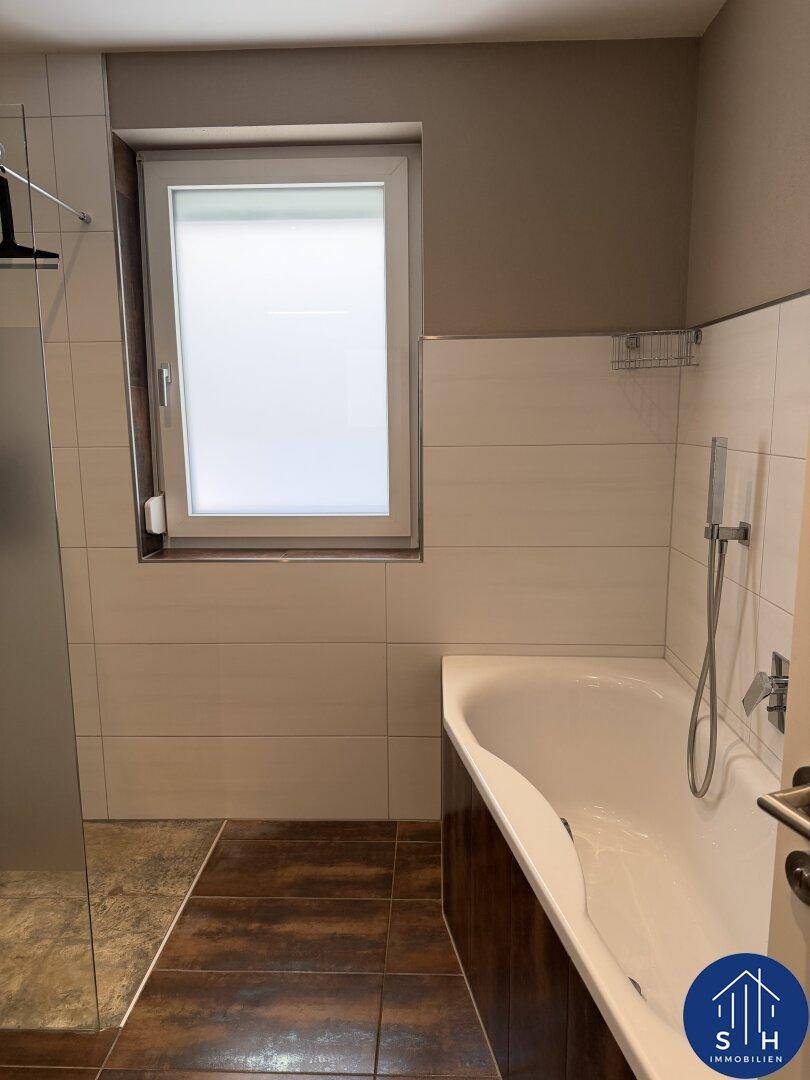 Modernes Badezimmer mit Badewanne, Duschbereich und einem Fenster für Tageslicht.