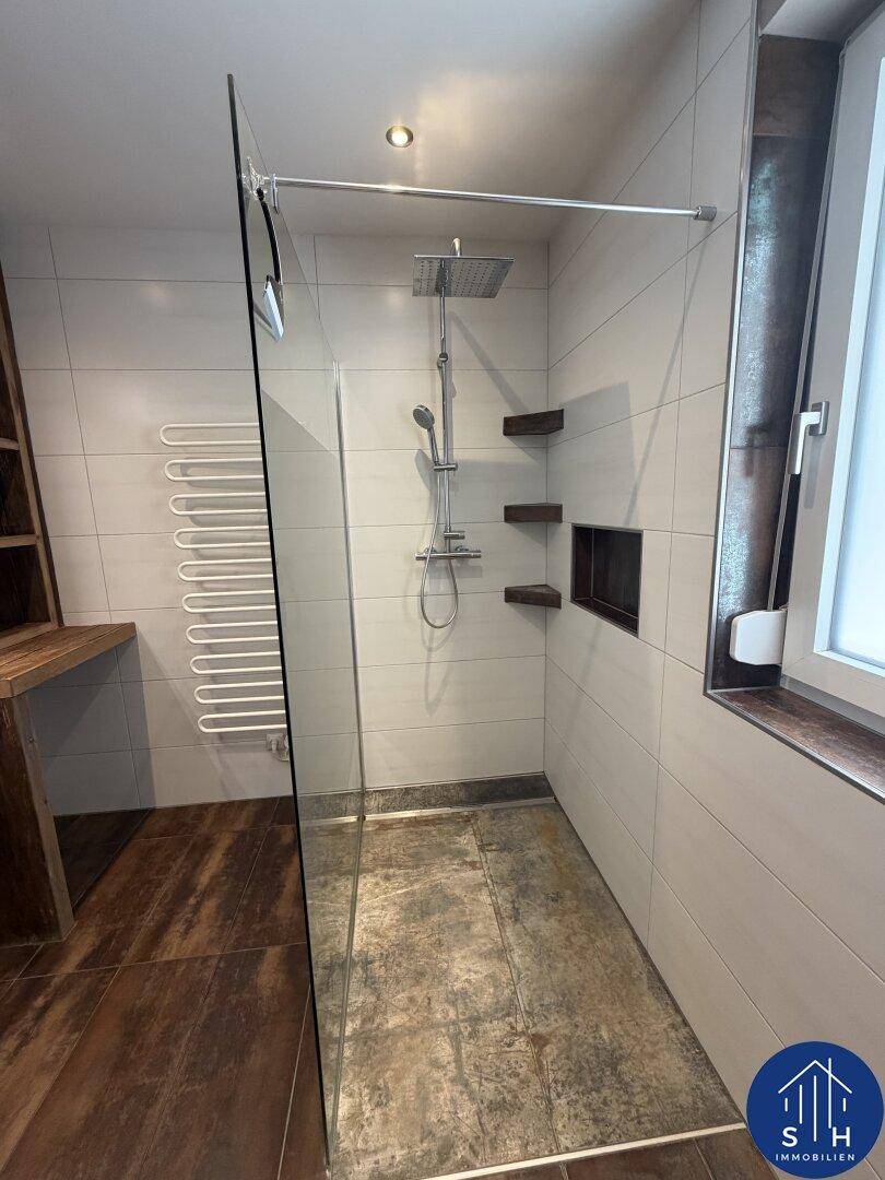 Moderne begehbare Dusche mit Regenduschkopf und praktischen Ablagen in der Wand.
