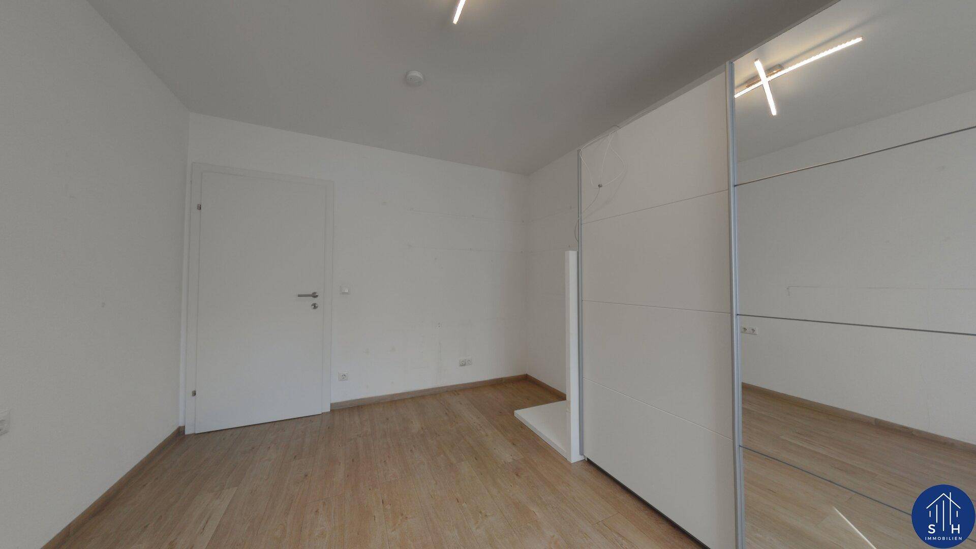 Helles Schlafzimmer mit Parkettboden und einem großen Spiegelschrank, der den Raum optisch vergrößert.