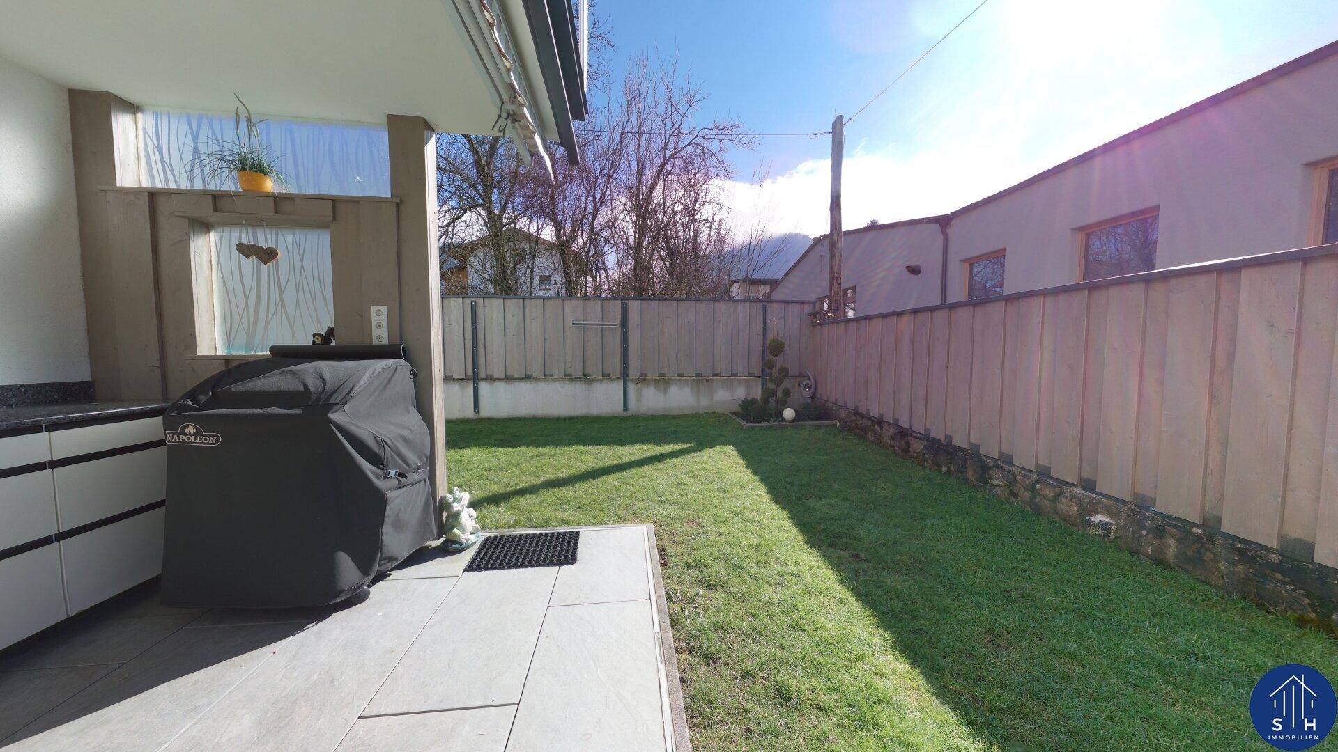 Gepflegter Gartenbereich mit Rasenfläche, Außenküche und Grillplatz, ideal für Sommerabende.