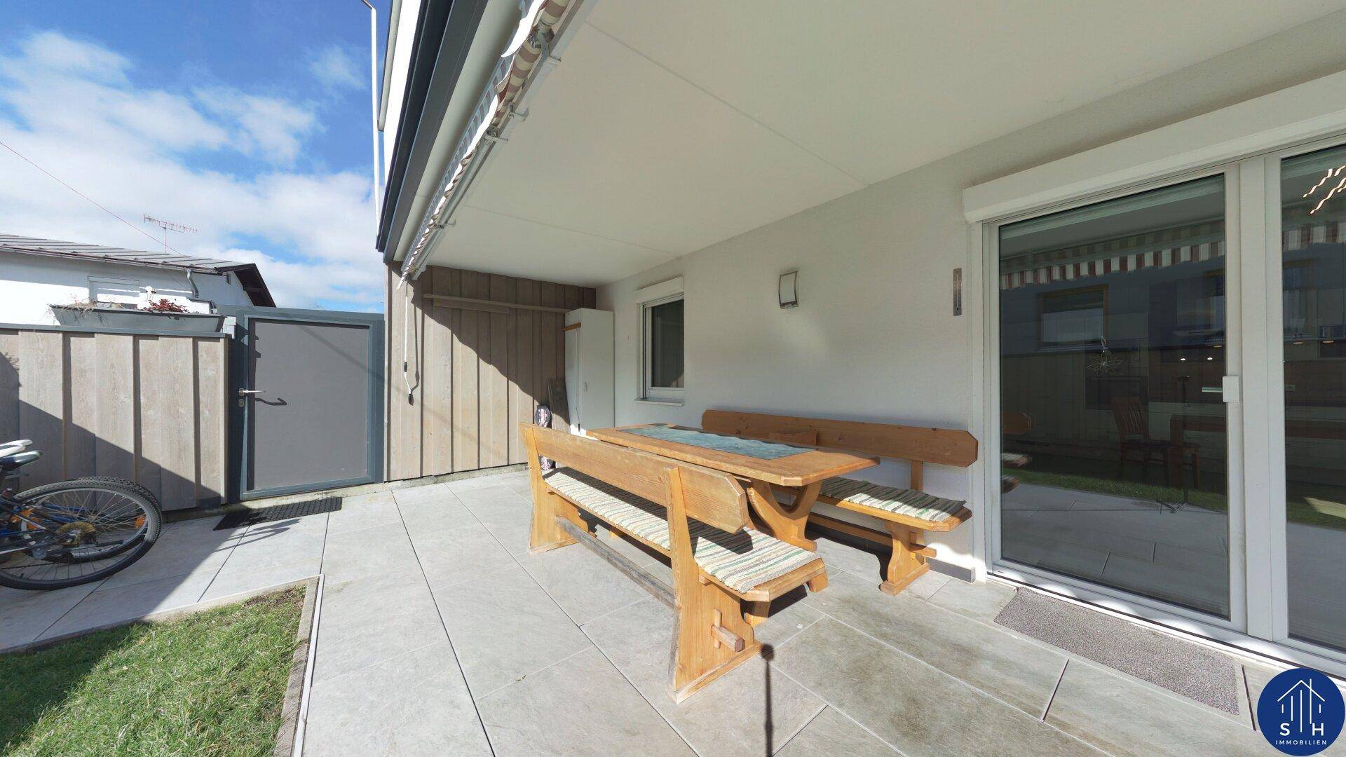Gepflasterte Terrasse mit rustikalen Holzmöbeln und Zugang zum Haus, ideal für Mahlzeiten im Freien.