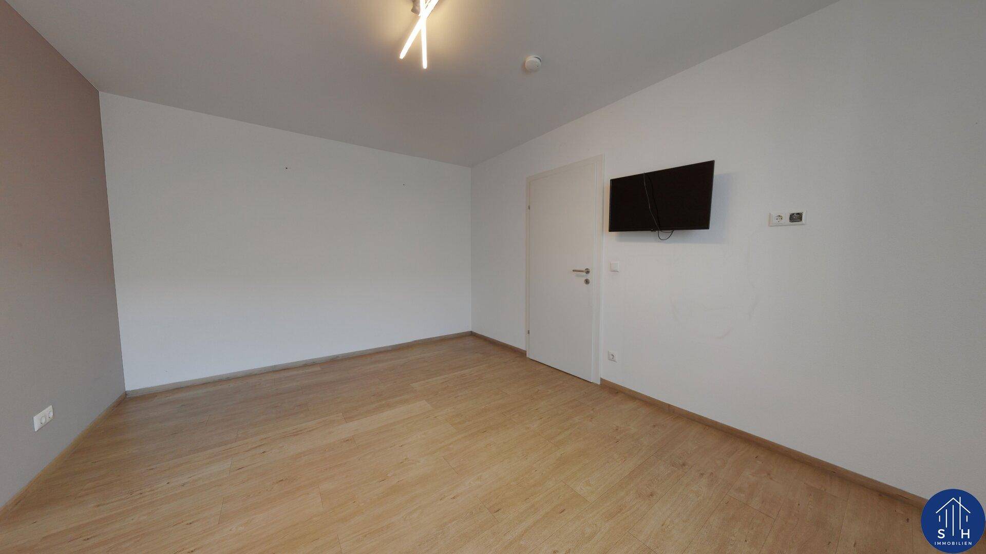 Geräumiges Schlafzimmer mit hellem Holzboden und einer Wandhalterung für einen Fernseher.