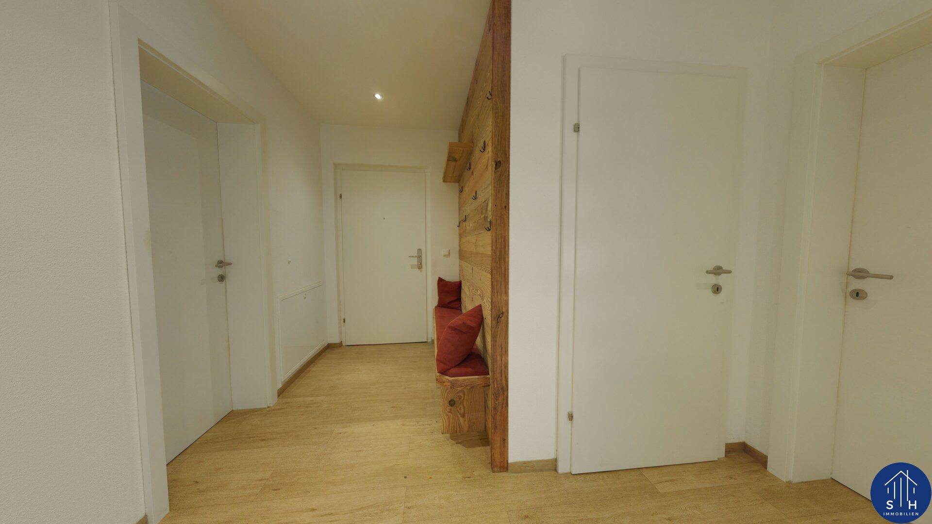 Heller Flur mit Holzboden und einer einladenden Holzsitzbank mit roten Kissen.