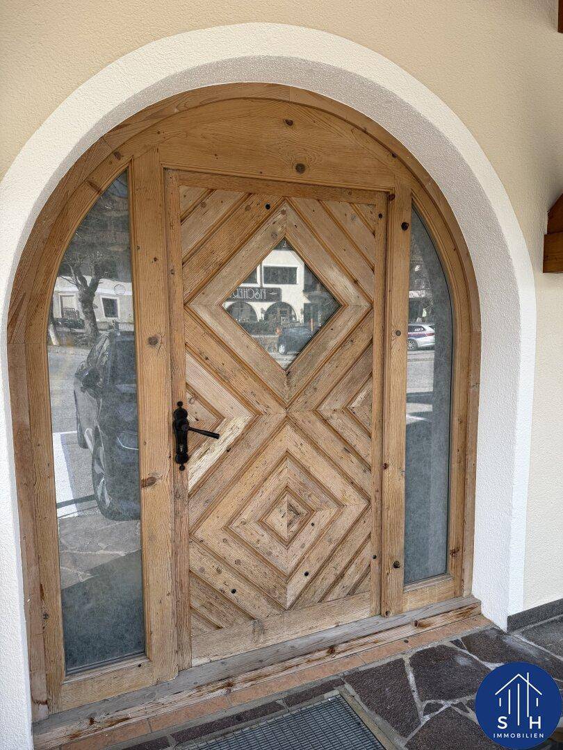 Rustikale Holztür mit Rautenmuster und seitlichen Glaseinsätzen in einem Rundbogen.