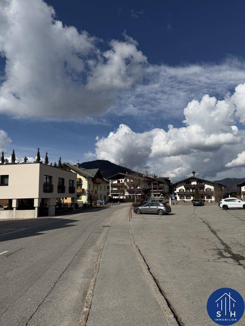 Weitläufige Straße mit Gebäuden im traditionellen Stil und Bergen im Hintergrund unter blauem Himmel.
