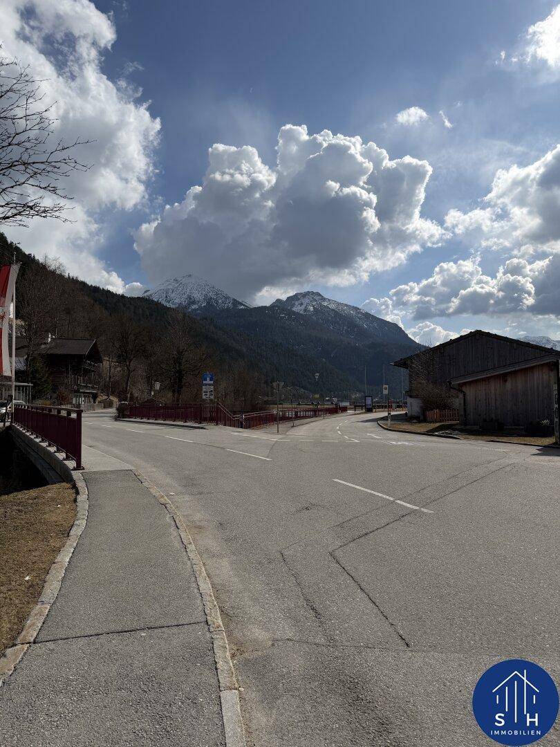Panoramablick auf eine Berglandschaft mit Straße und traditionellen Gebäuden unter bewölktem Himmel.