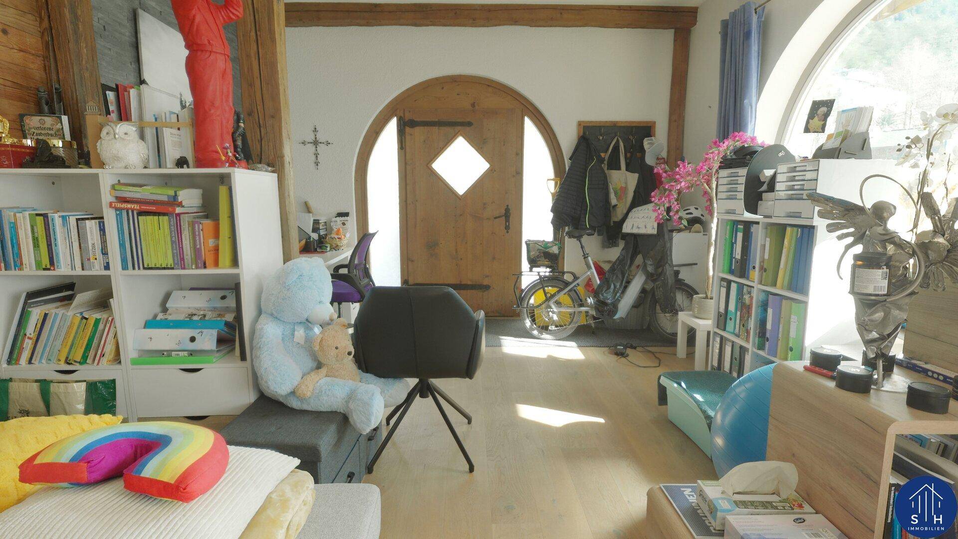 Geräumiger Wohnbereich mit Holzelementen, Bücherregal und einem Blick auf den Eingangsbereich.