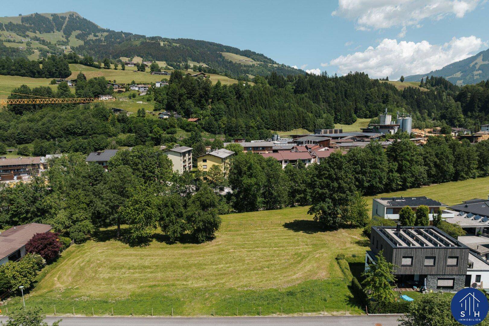 Panoramablick auf ein Dorf eingebettet in grüne Hügel und Wälder unter blauem Himmel.