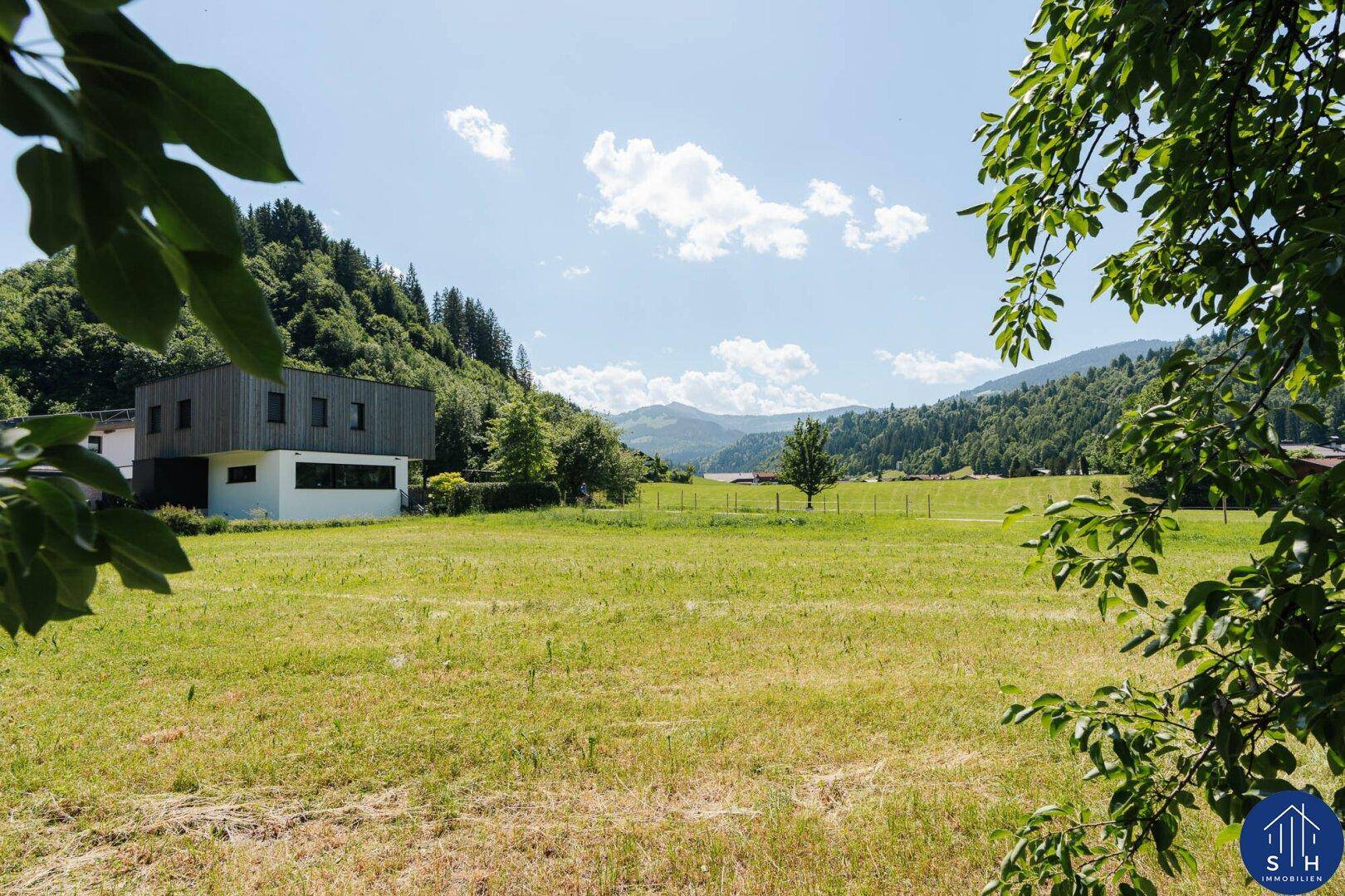 Modernes Gebäude neben einer weiten Wiese mit Blick auf die umliegende Berglandschaft.