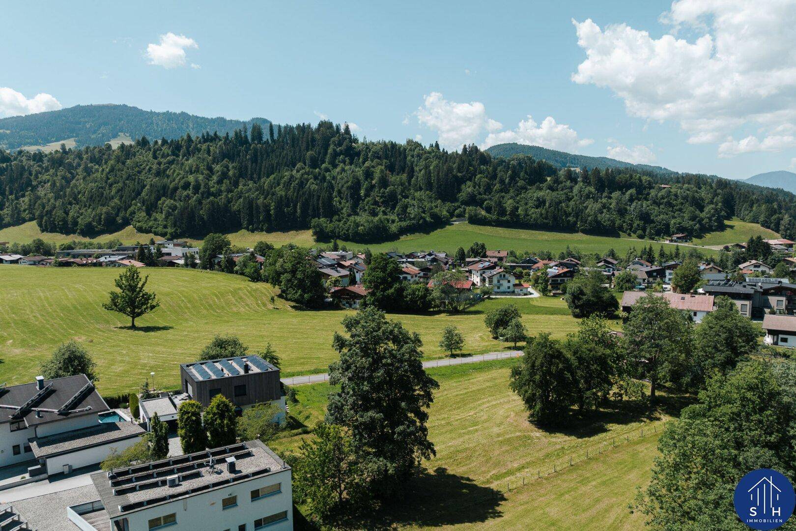 Luftaufnahme eines Dorfes mit grünen Feldern und Wohnhäusern in einer idyllischen Landschaft.