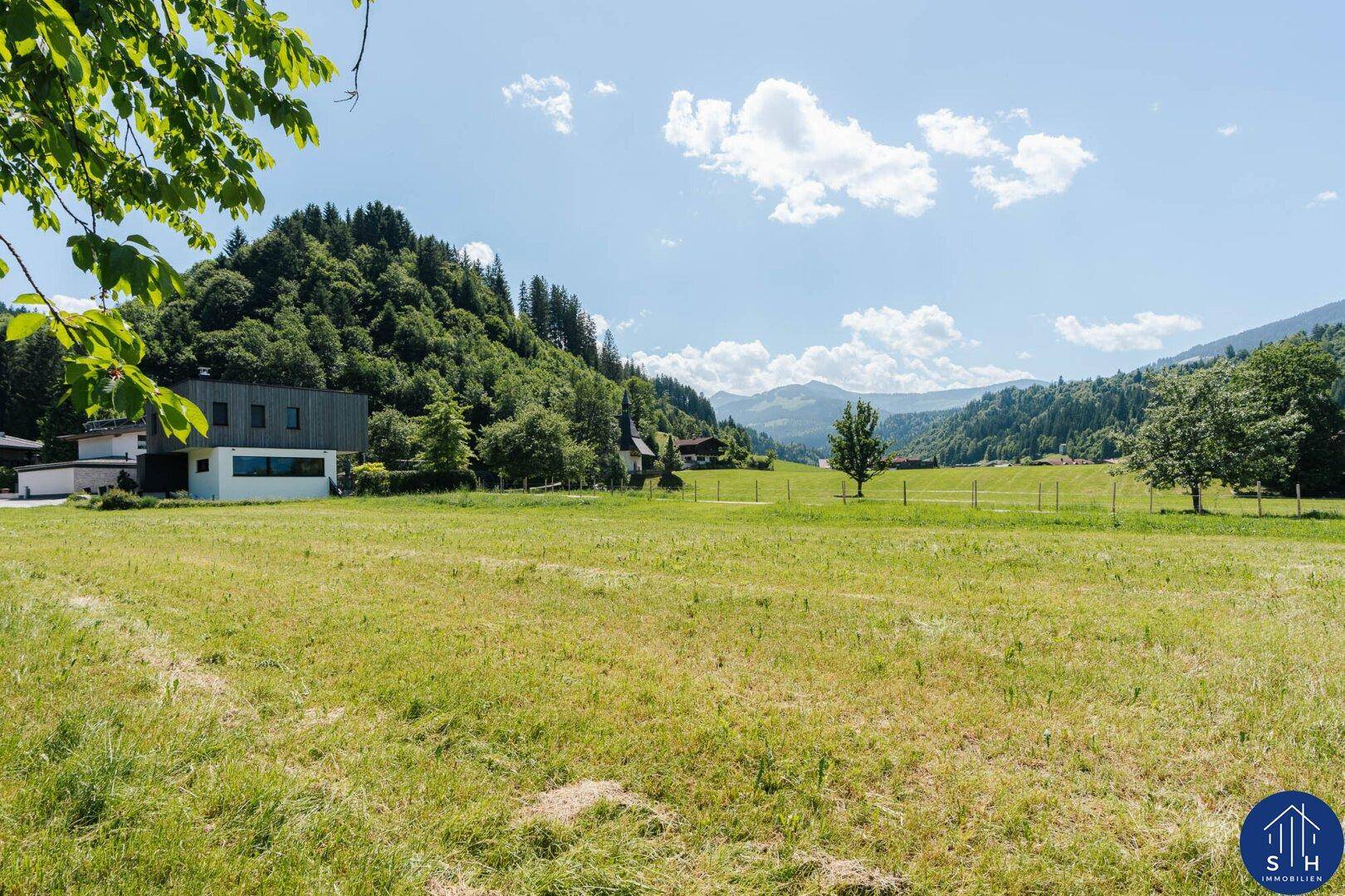 Modernes Haus an einer grünen Wiese mit malerischem Blick auf die umliegenden Berge.