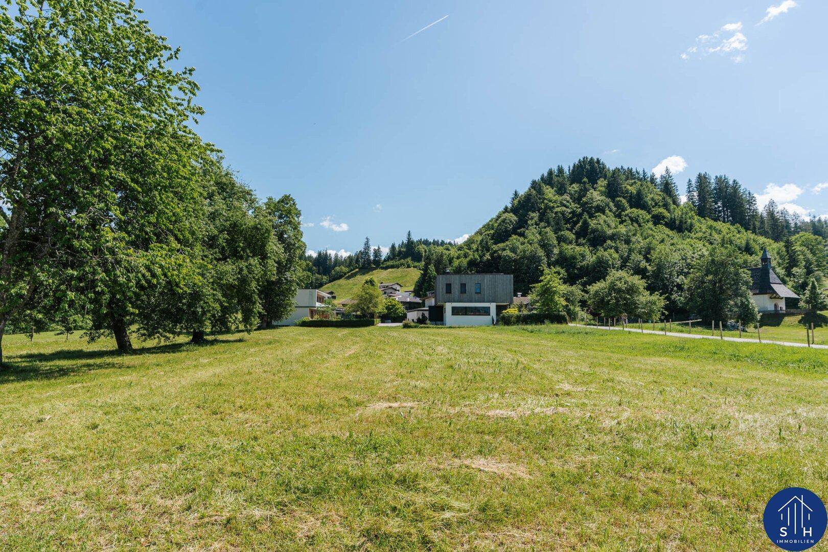 Weitläufige Wiese mit modernem Gebäude und einer Kirche im Hintergrund.