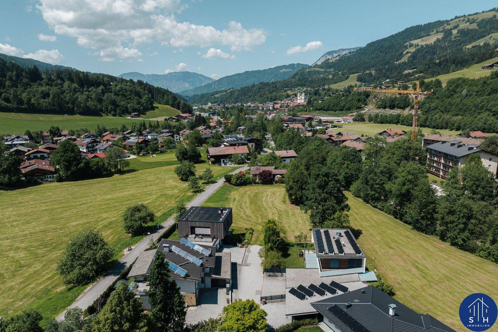 Luftaufnahme eines Dorfes in einem grünen Tal mit modernen Gebäuden und Bergen.