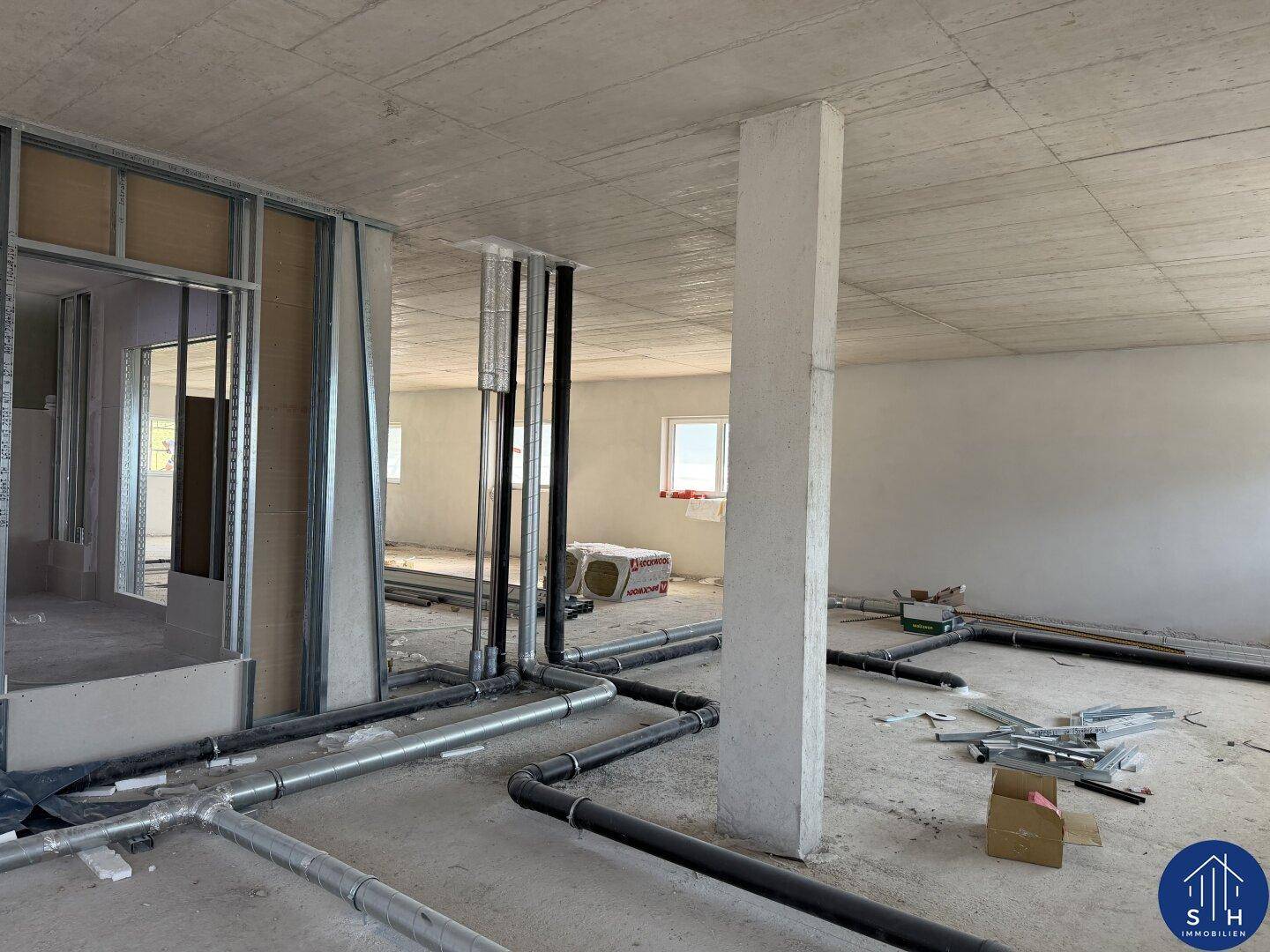 Innenraum im Rohbau mit sichtbaren Rohren, Leitungen und Metallständerwerk für zukünftige Wände.