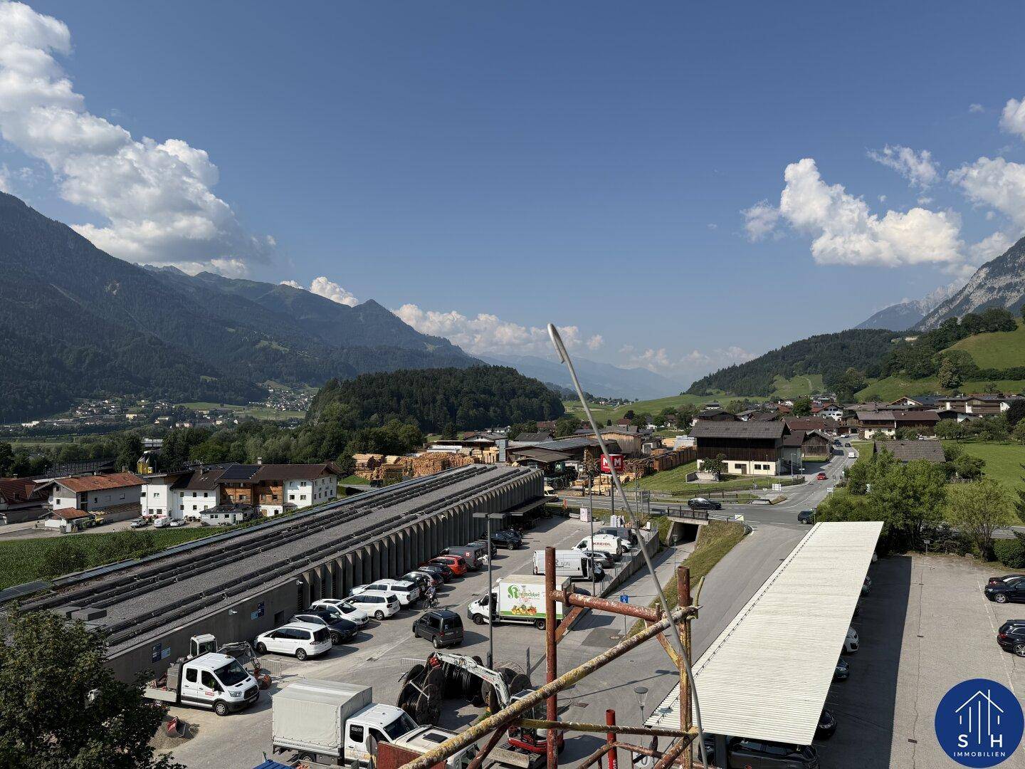 Panoramablick auf eine Berglandschaft mit einem Parkplatz und einer Straße im Vordergrund an einem sonnigen Tag.