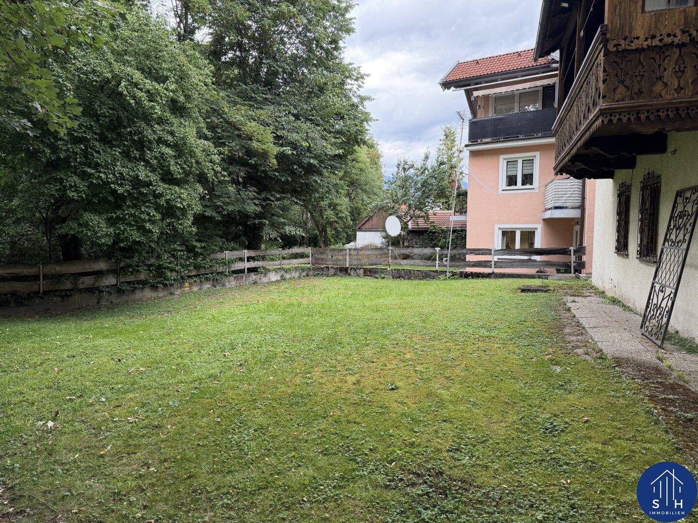 Großer, gepflegter Rasenbereich im Garten hinter dem Haus, umgeben von Bäumen und einem Holzzaun.