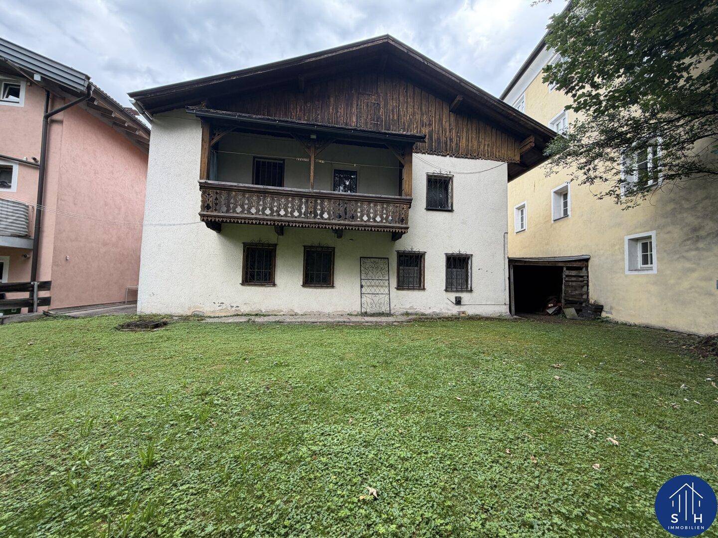 Rückansicht des Hauses mit traditionellem Holzbalkon und einem weitläufigen, grünen Gartenbereich.