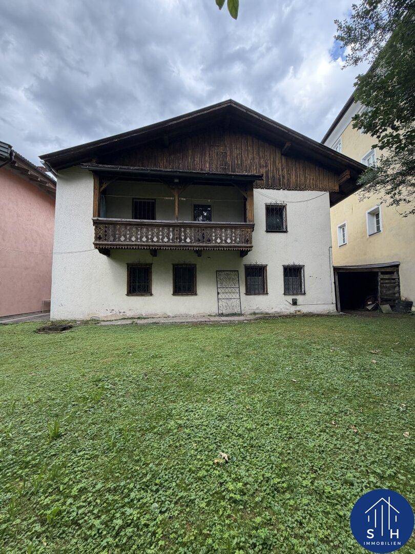 Das Haus von hinten mit einem großen Rasen und einem traditionellen Holzbalkon unter bewölktem Himmel.