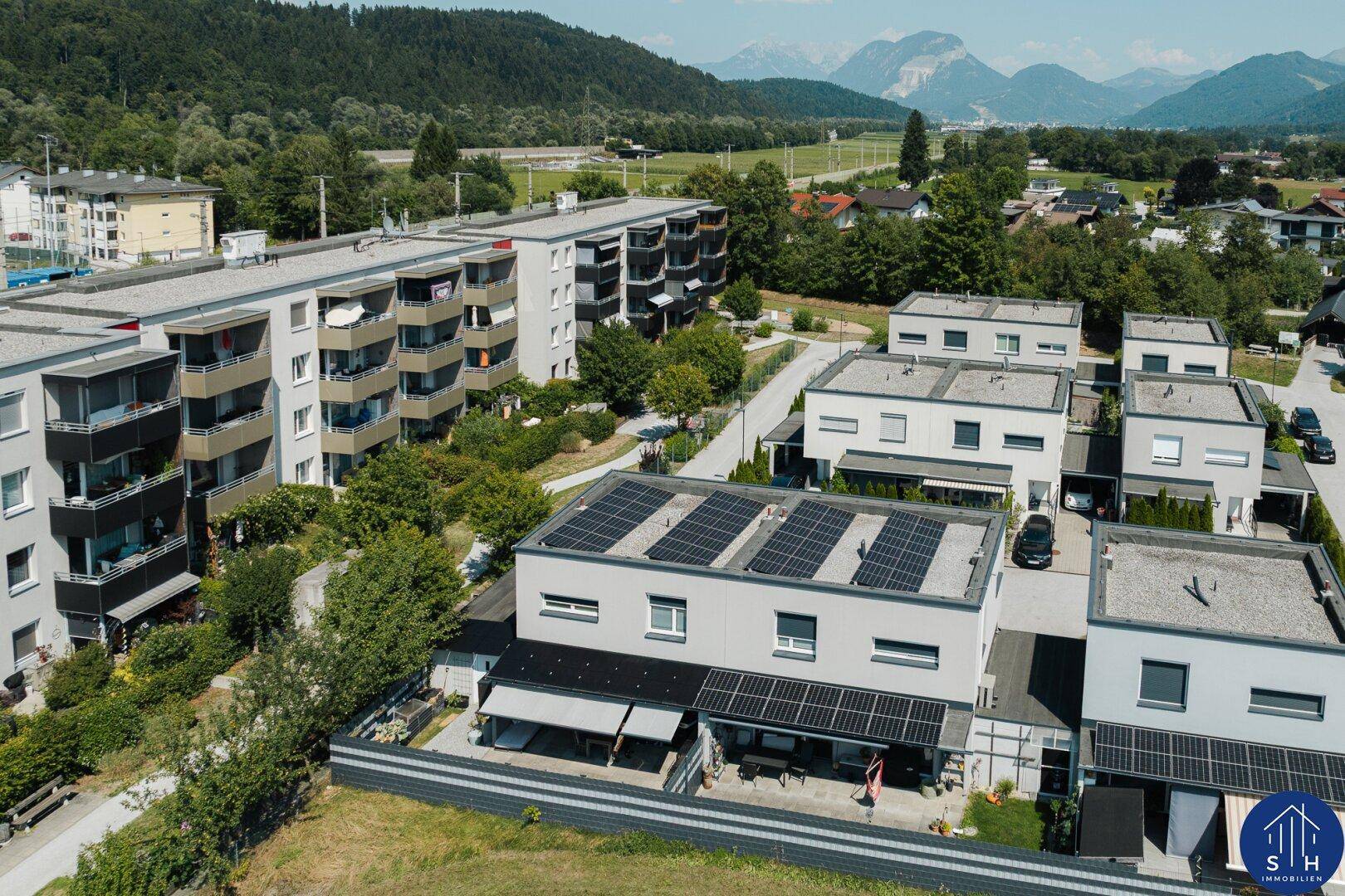 Luftaufnahme moderner Wohnhäuser mit Photovoltaikanlagen auf den Dächern und Bergblick.