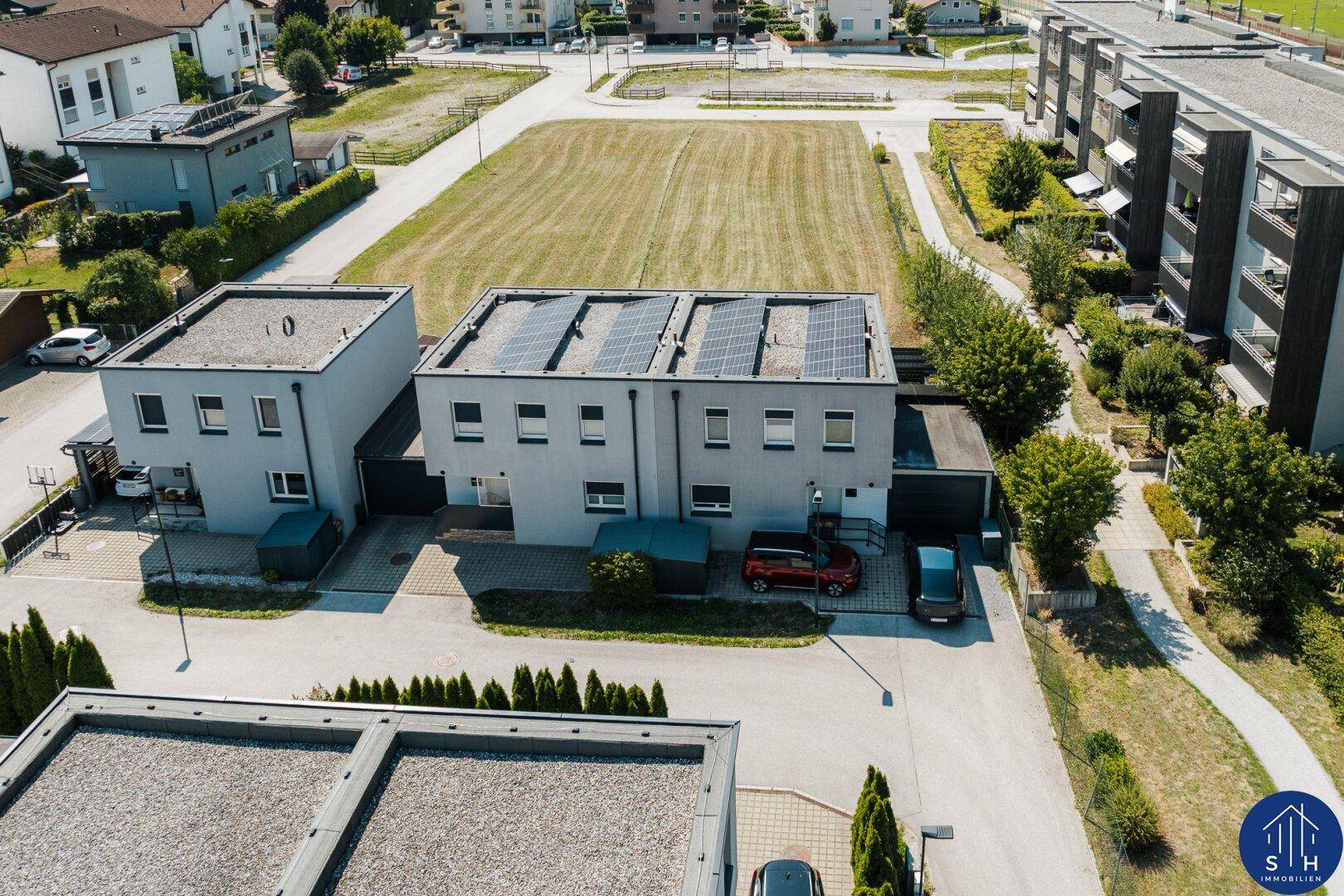 Luftaufnahme von zwei modernen Häusern mit Solarpaneelen auf dem Dach und angrenzenden Freiflächen.