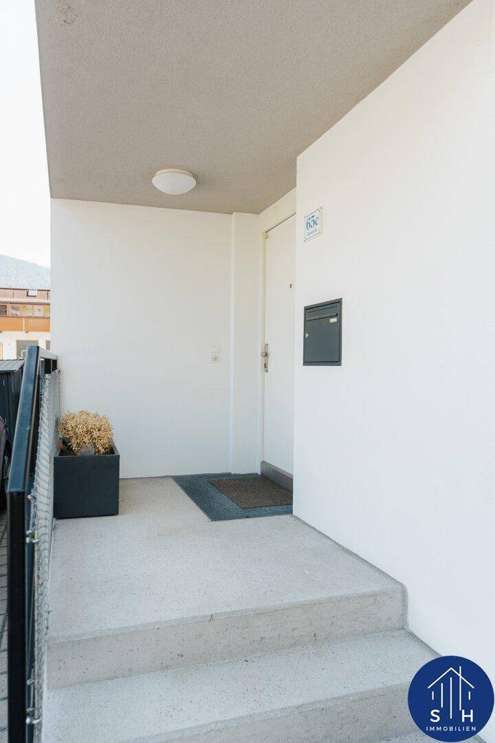 Eingangsbereich des Hauses mit Betontreppe und weißer Haustür unter einem Vordach.