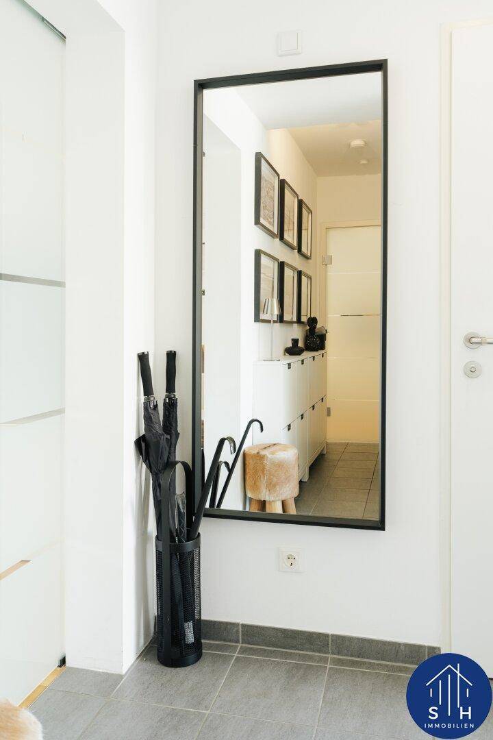 Eingangsbereich mit großem Wandspiegel, Schuhschrank und grauen Bodenfliesen.