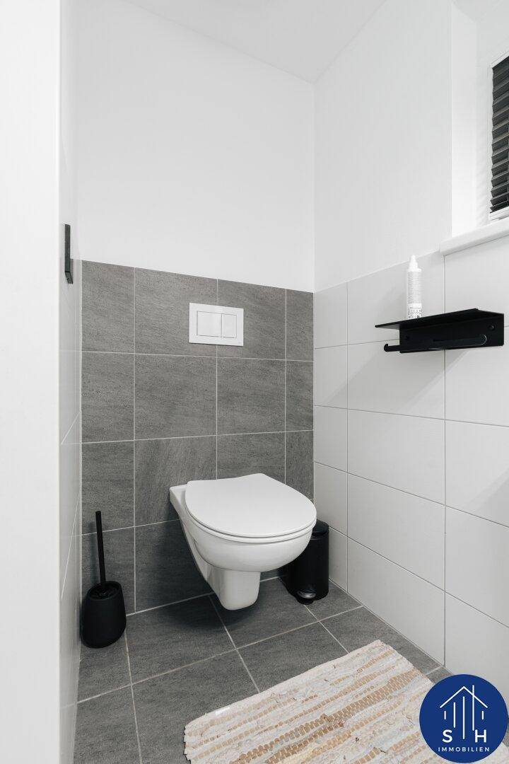 Modernes Gäste-WC mit wandhängender Toilette und stilvollen Grau-Weiß-Fliesen.