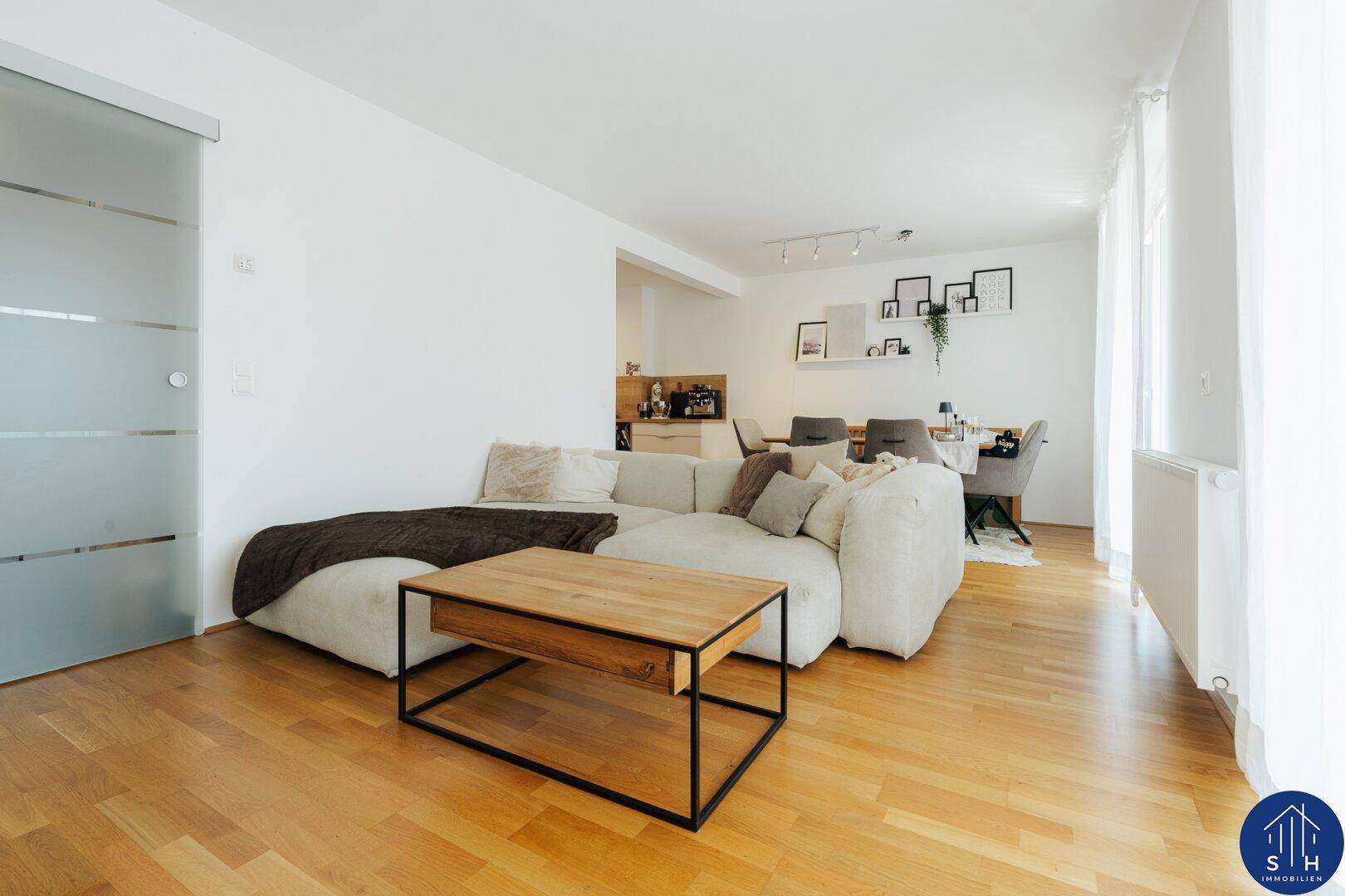Geräumiger Wohnbereich mit beigem Sofa, Holztisch und moderner Glasschiebetür zum Essbereich.
